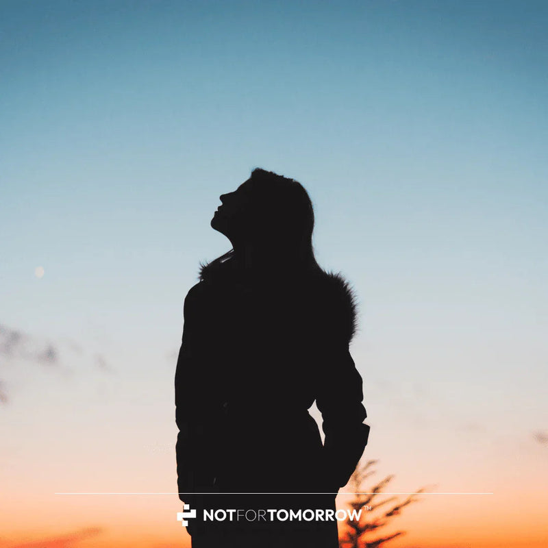 Silhouette of woman looking up at sunset sky, inspiration and wellness concept