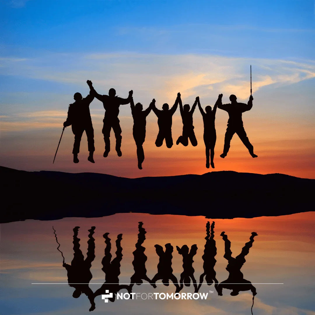Silhouettes of six people holding hands and jumping at sunset, reflected in water.