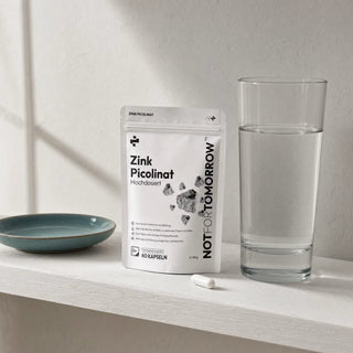 Zink Picolinaat pouch on a white shelf beside a glass of water, ceramic dish and one white capsule