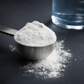 Steel scoop heaped with white NOTFORTOMORROW creatine monohydrate powder beside a glass of water on slate
