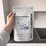 NOTFORTOMORROW Kreatinmonohydrat 500 g pose holdt oppe af én hånd i et ryddeligt hjemmekøkken