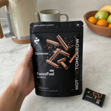 NOTFORTOMORROW FocusFuel Cinnamon, påse med 60 dospåsar hållen i en hand i ett rent kök, en dospåse på diskbänken