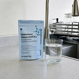 NOTFORTOMORROW Molecular Hydrogen tablet pouch on a kitchen counter behind a glass of sparkling water