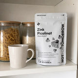 NOTFORTOMORROW Zink Picolinaat zak met 120 capsules op een keukenkastplank naast een mok en glazen potten met pasta en rijst