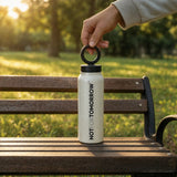 NOTFORTOMORROW MAGBOTL vanilla white water bottle on park bench with grass in soft focus, hand picks up by ring lid