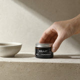 NOTFORTOMORROW Shilajit amber jar on light stone shelf beside a small ceramic bowl, hand places the jar