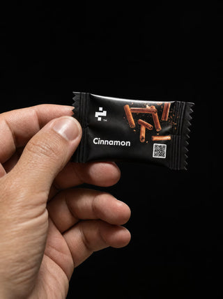 Hand holding a single NOTFORTOMORROW FocusFuel Cinnamon sachet against a black background